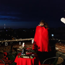 A couple on a rooftop, wrapped in a blanket, surrounded by a romantic arrangement.