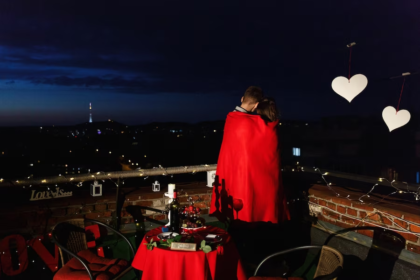 A couple on a rooftop, wrapped in a blanket, surrounded by a romantic arrangement.