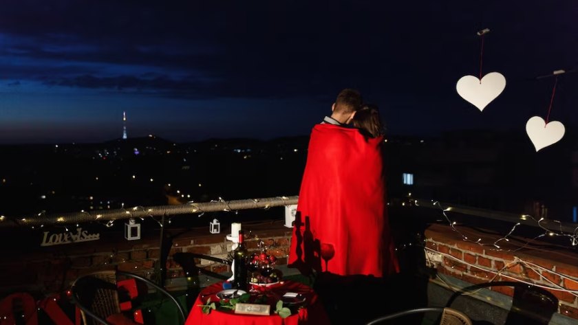 A couple on a rooftop, wrapped in a blanket, surrounded by a romantic arrangement.