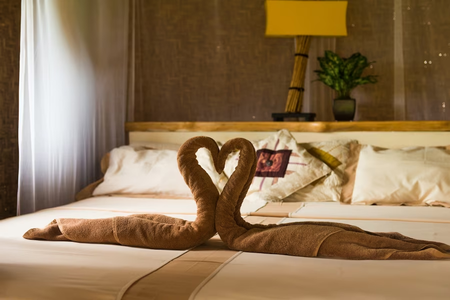 Hotel bed adorned with a swan-shaped towel artfully crafted into a heart shape, placed on the bed's surface.