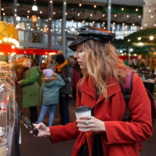 Girl in red coat and hat capturing a cake outdoor Christmas bazaar.