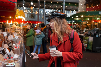 Girl in red coat and hat capturing a cake outdoor Christmas bazaar.