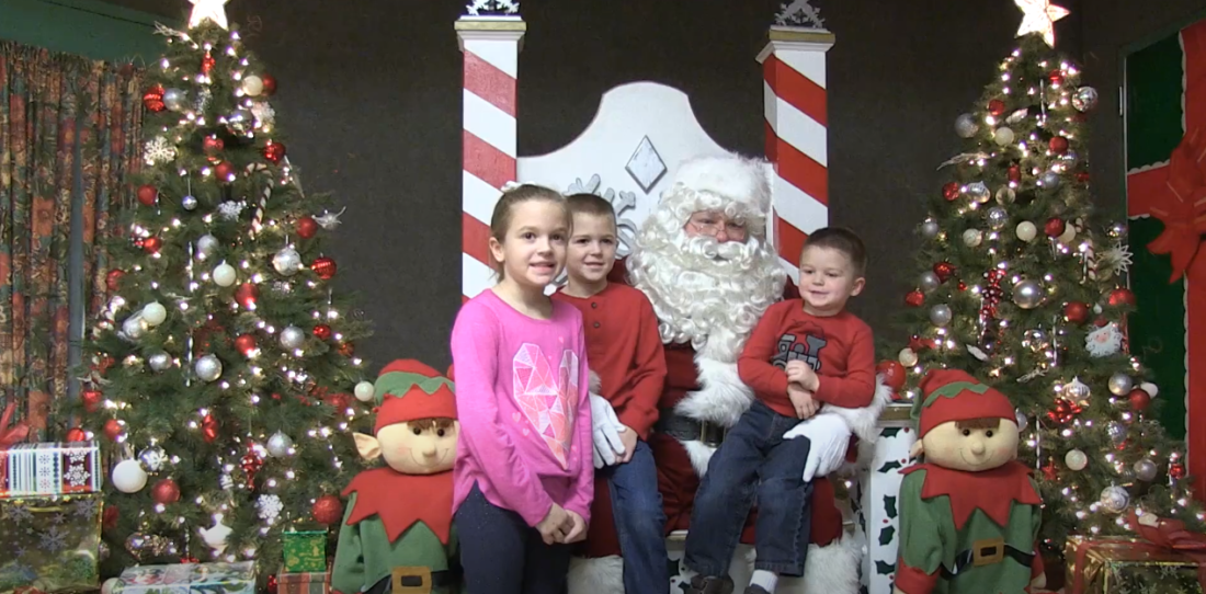 Children with Santa, presents, and a nearby Christmas tree.