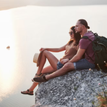 hugging couple sitting on top of rock mountain and watching on sunset