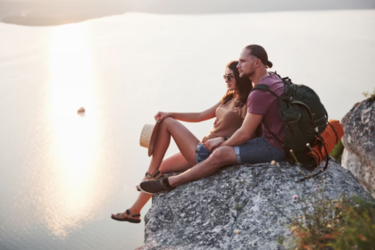 hugging couple sitting on top of rock mountain and watching on sunset