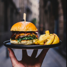 a hand holding a burger with fried potato slices on a black plate