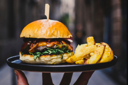 a hand holding a burger with fried potato slices on a black plate