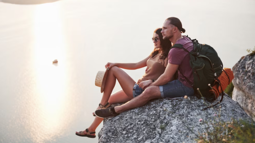 hugging couple sitting on top of rock mountain and watching on sunset