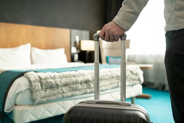 person holding suitcase with blurred bed in background