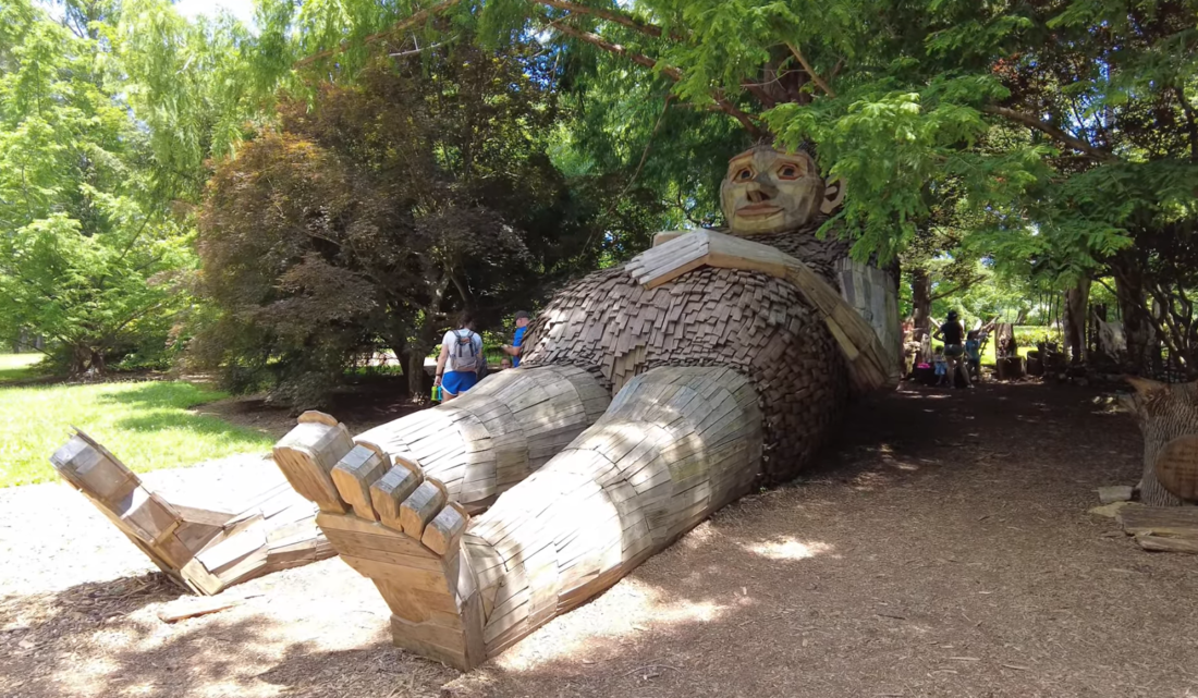 lying wooden giant in the forest and people near it under the trees