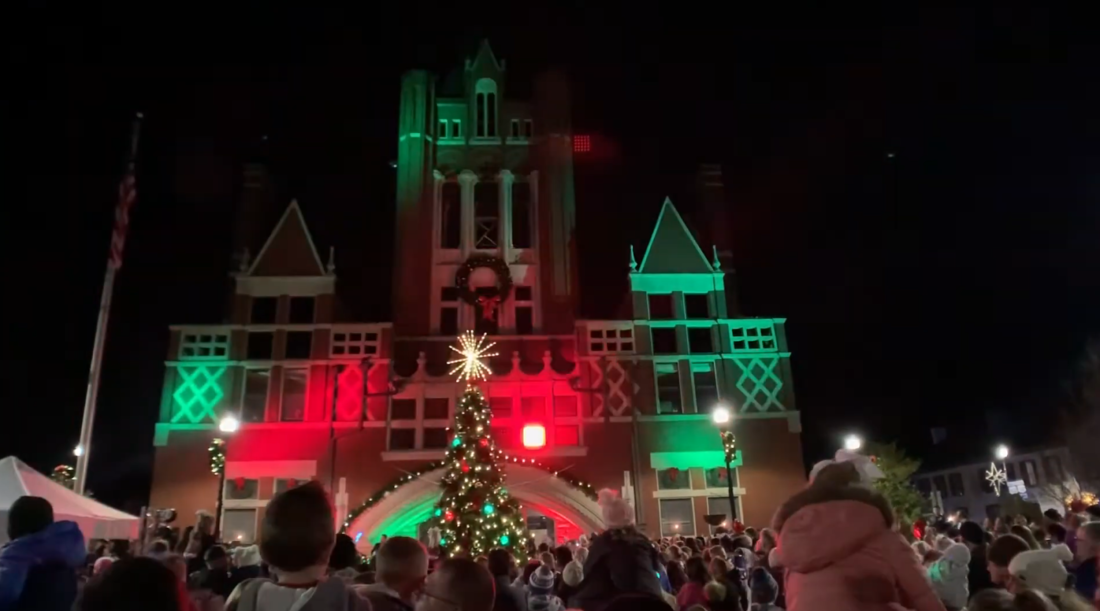 building and New Year tree near it, people standings and watching on it